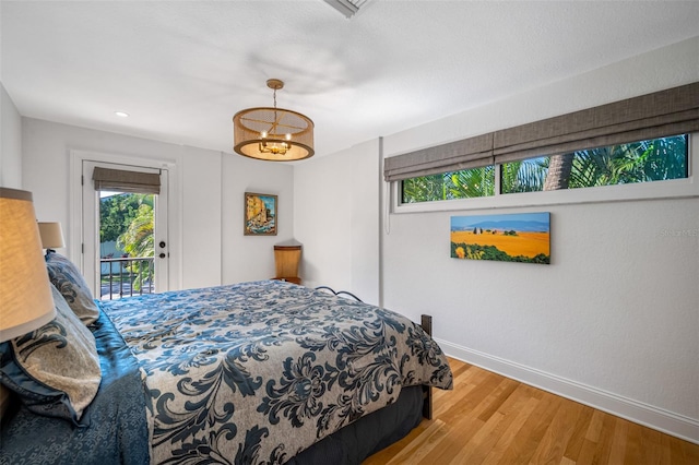 bedroom featuring access to exterior, a notable chandelier, and hardwood / wood-style flooring