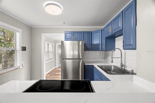 kitchen featuring blue cabinetry, decorative backsplash, stainless steel fridge, and sink