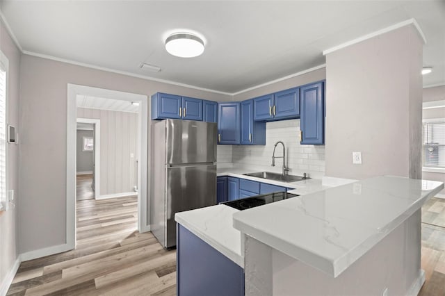 kitchen featuring sink, backsplash, kitchen peninsula, stainless steel fridge, and ornamental molding