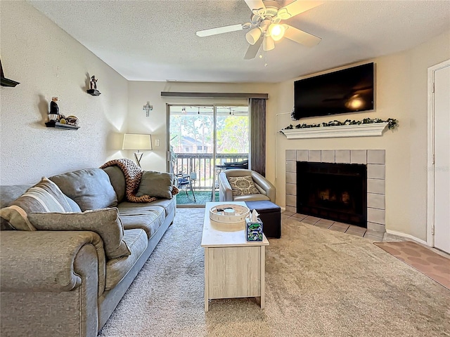 carpeted living room with ceiling fan, a tile fireplace, and a textured ceiling