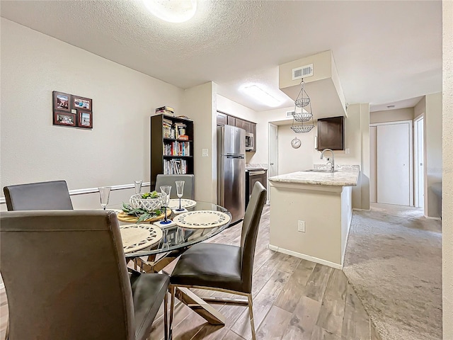 dining room with sink, light hardwood / wood-style flooring, and a textured ceiling