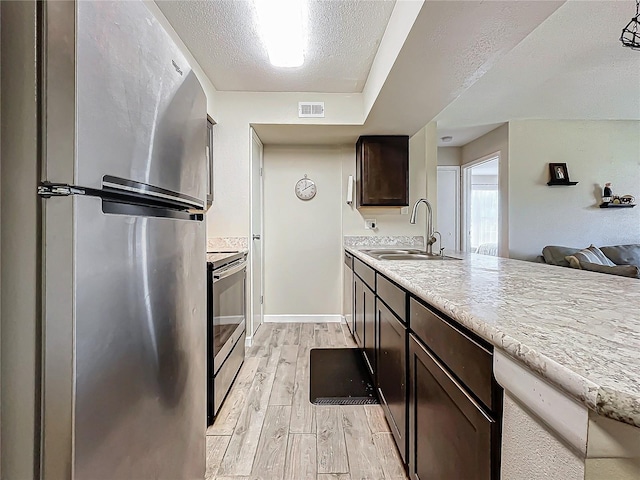 kitchen featuring sink, dark brown cabinets, a textured ceiling, light wood-type flooring, and stainless steel appliances