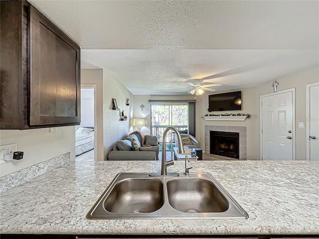 kitchen featuring dark brown cabinetry, a tiled fireplace, sink, and a textured ceiling