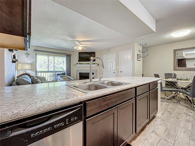 kitchen featuring a tiled fireplace, sink, dark brown cabinets, and stainless steel dishwasher