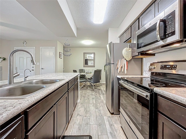 kitchen featuring dark brown cabinetry, sink, light hardwood / wood-style flooring, a textured ceiling, and stainless steel appliances