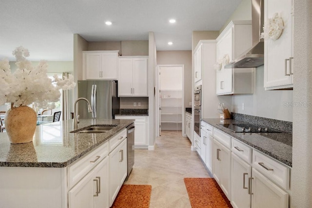 kitchen with dark stone counters, wall chimney exhaust hood, stainless steel appliances, sink, and white cabinetry