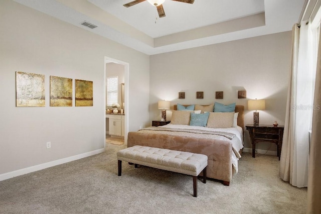 bedroom with ceiling fan, light carpet, connected bathroom, and a tray ceiling