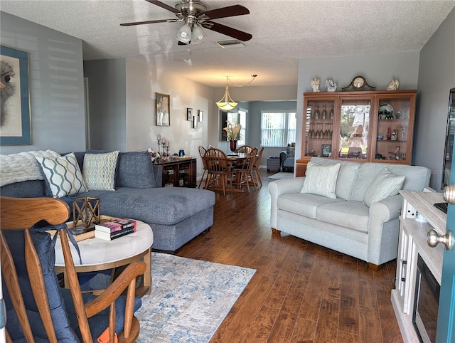 living room with dark wood-type flooring, ceiling fan, and a textured ceiling