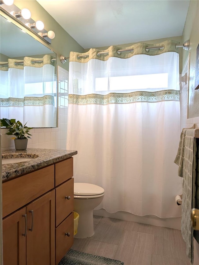 bathroom with a shower with curtain, vanity, toilet, and tile walls