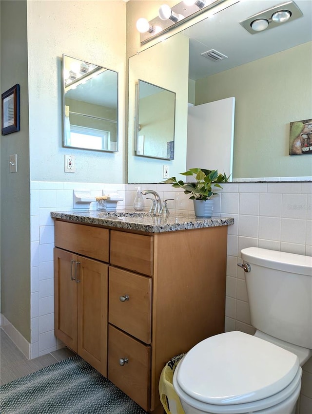 bathroom featuring vanity, tile walls, and toilet