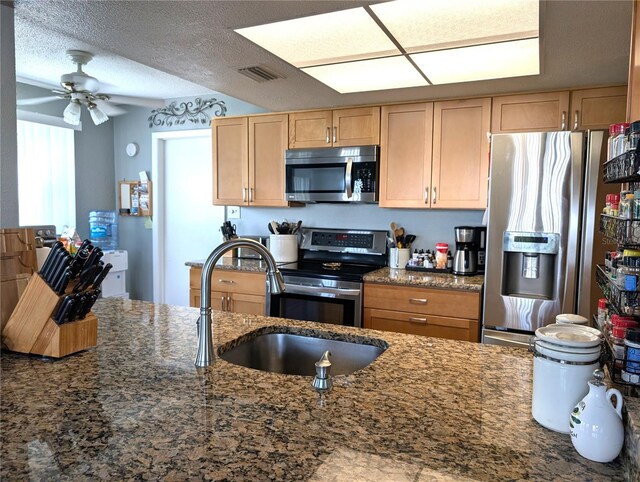 kitchen with sink, ceiling fan, appliances with stainless steel finishes, dark stone countertops, and a textured ceiling