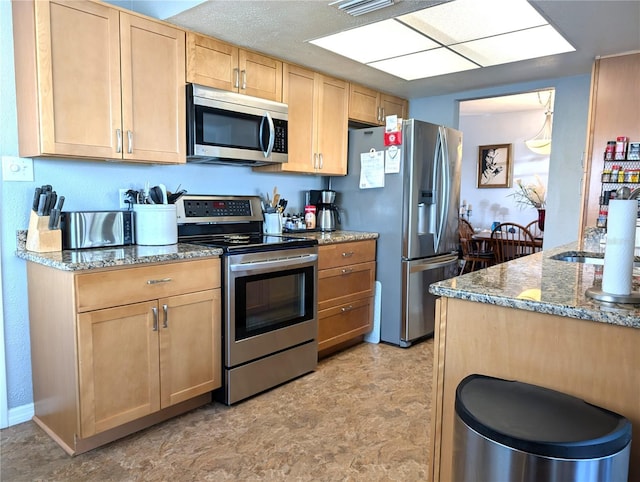 kitchen with light brown cabinetry, sink, dark stone counters, and appliances with stainless steel finishes