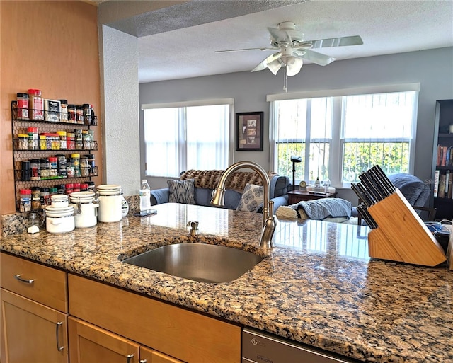 kitchen with stone counters, ceiling fan, sink, and a textured ceiling