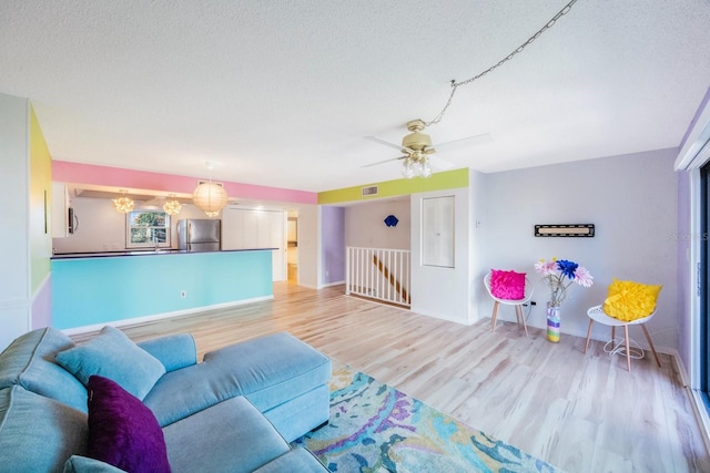 living room featuring ceiling fan, a textured ceiling, and light wood-type flooring