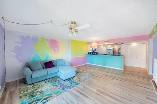 living room with ceiling fan, a textured ceiling, and light wood-type flooring