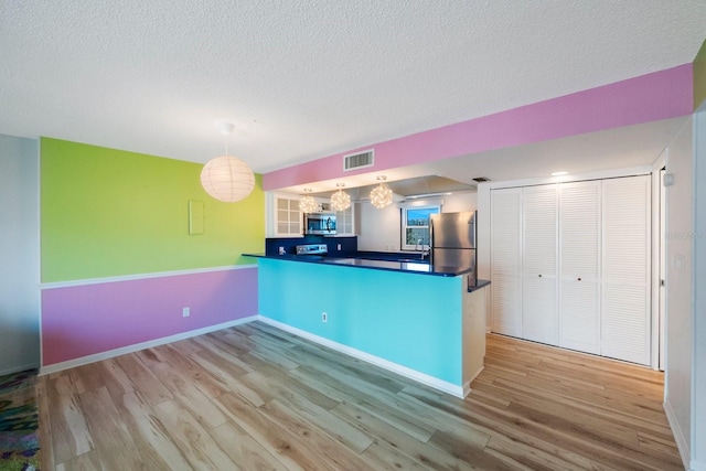 kitchen with pendant lighting, light wood-type flooring, kitchen peninsula, and appliances with stainless steel finishes