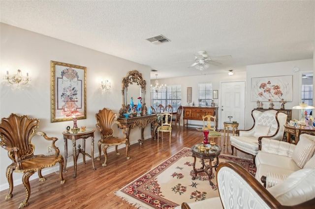 living area featuring plenty of natural light, ceiling fan with notable chandelier, a textured ceiling, and hardwood / wood-style flooring