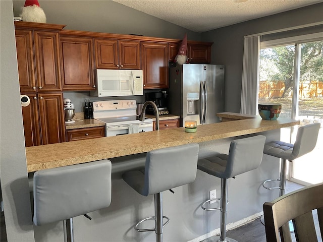 kitchen with kitchen peninsula, lofted ceiling, a breakfast bar, and white appliances