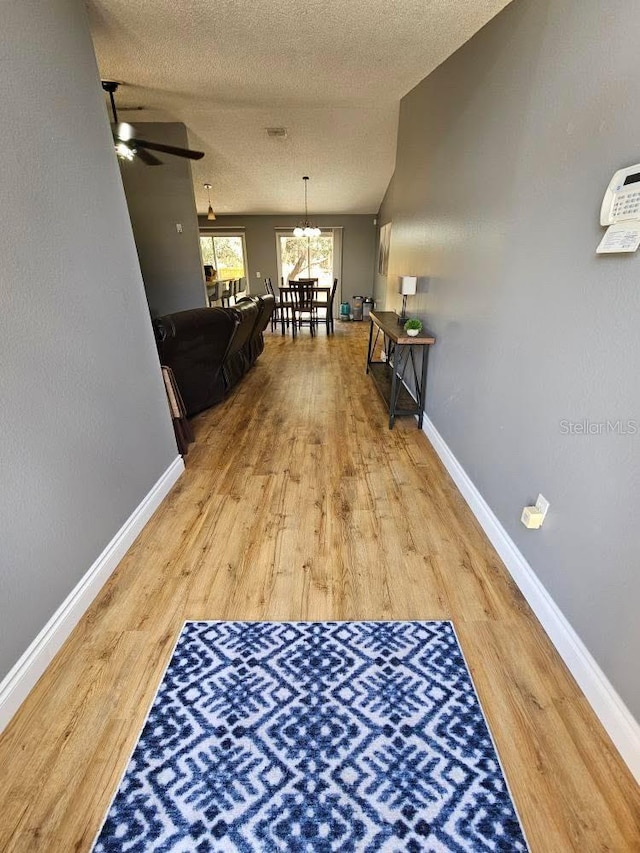 hall featuring a textured ceiling, baseboards, and wood finished floors