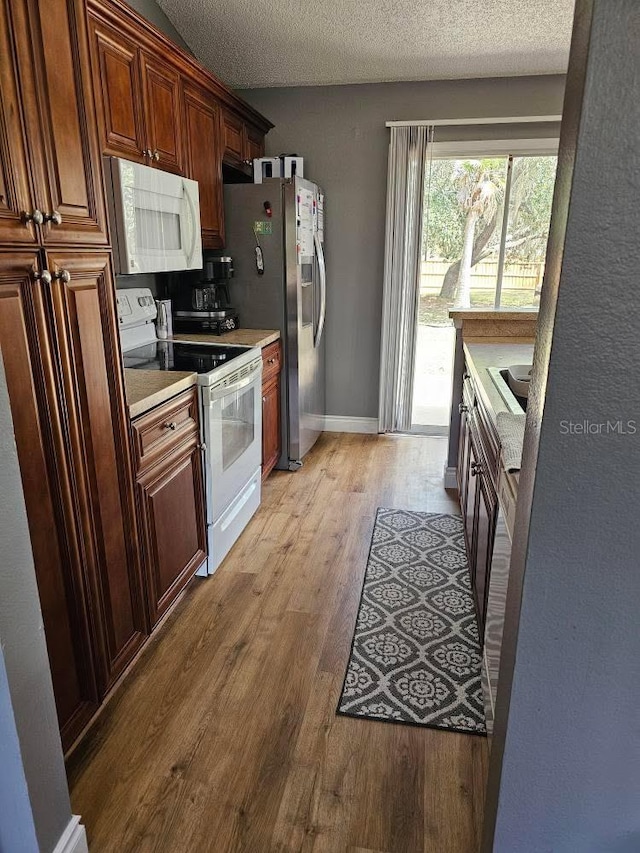 kitchen with light countertops, light wood-type flooring, white appliances, baseboards, and a textured ceiling