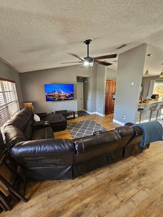living area featuring lofted ceiling, wood finished floors, ceiling fan, and a textured ceiling