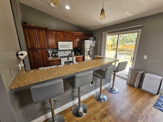 kitchen featuring vaulted ceiling, a sink, a kitchen bar, light wood-type flooring, and white appliances