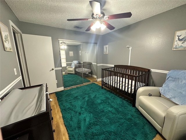 bedroom featuring a closet, a textured ceiling, visible vents, ceiling fan, and wood finished floors