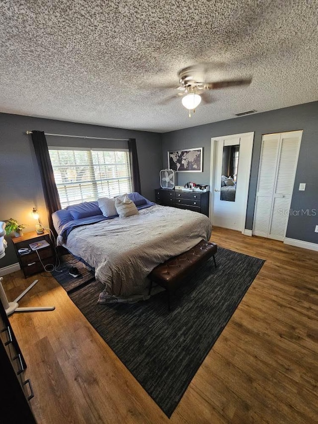 bedroom featuring a ceiling fan, wood finished floors, a textured ceiling, baseboards, and visible vents