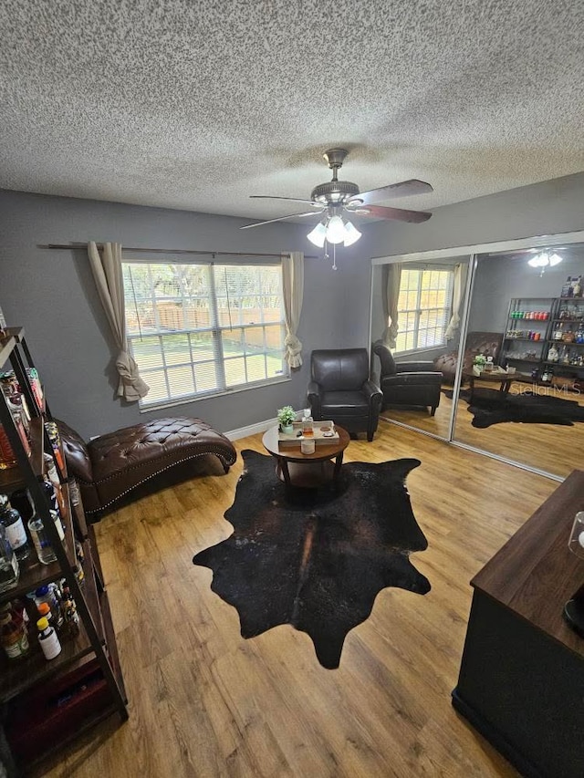 living room featuring a textured ceiling, a ceiling fan, wood finished floors, and a healthy amount of sunlight