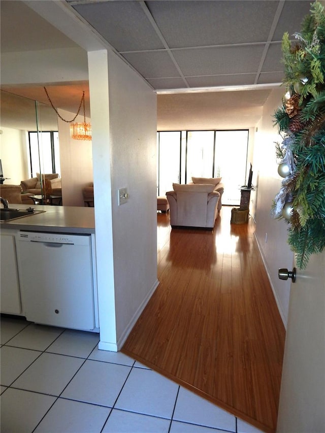 hall featuring light tile patterned floors, a paneled ceiling, a notable chandelier, and sink