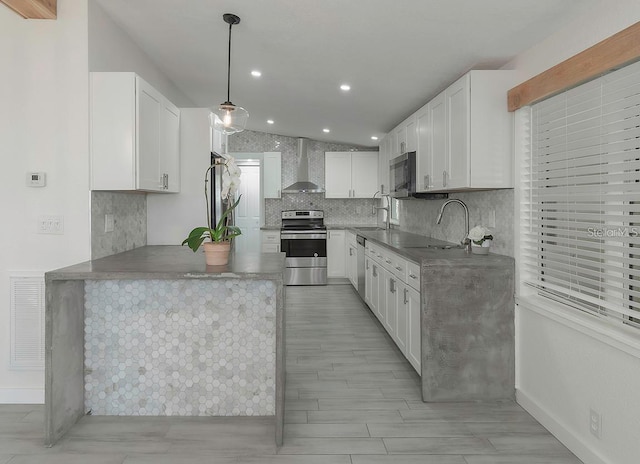 kitchen featuring appliances with stainless steel finishes, sink, wall chimney range hood, white cabinets, and hanging light fixtures