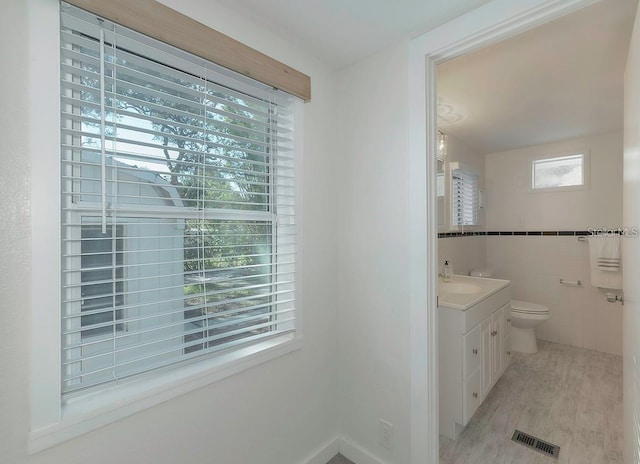 bathroom featuring vanity, a healthy amount of sunlight, toilet, and tile walls