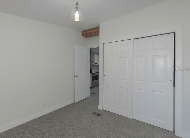 unfurnished bedroom featuring beamed ceiling, light colored carpet, and a closet