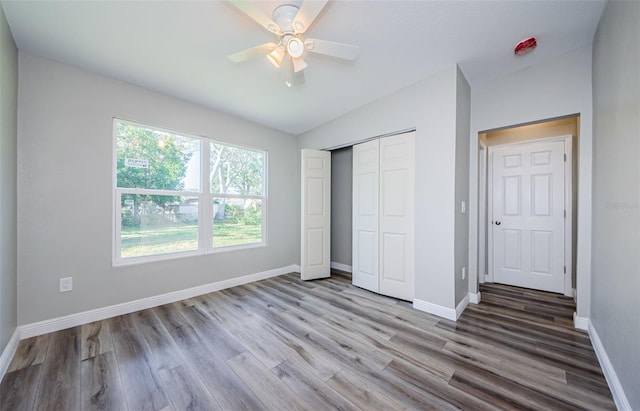 unfurnished bedroom featuring baseboards, lofted ceiling, ceiling fan, wood finished floors, and a closet