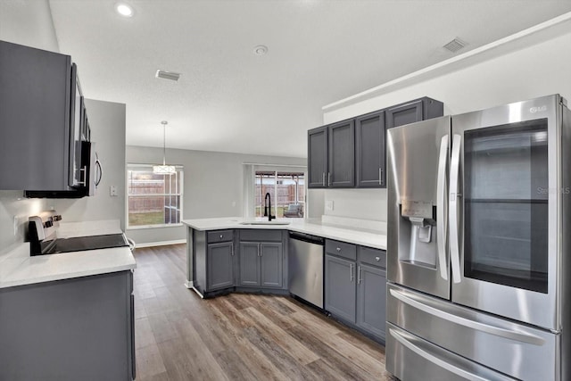 kitchen with sink, dark hardwood / wood-style floors, kitchen peninsula, pendant lighting, and appliances with stainless steel finishes