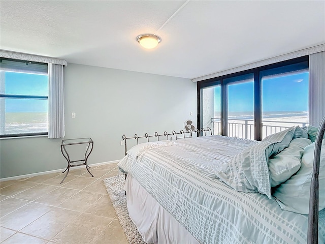 tiled bedroom with a water view, a textured ceiling, and a view of the beach