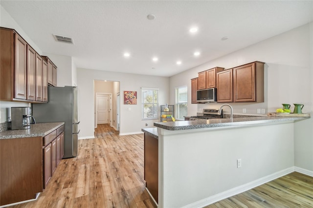 kitchen with light wood-type flooring, kitchen peninsula, sink, and appliances with stainless steel finishes