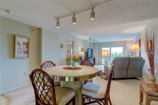 dining area with a textured ceiling, light carpet, and track lighting