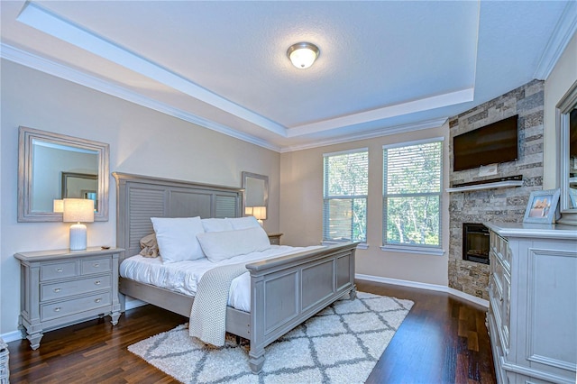 bedroom with dark hardwood / wood-style floors, a stone fireplace, a tray ceiling, and crown molding