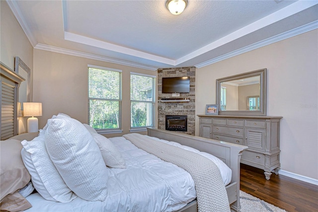 bedroom featuring dark hardwood / wood-style flooring, a textured ceiling, a tray ceiling, a fireplace, and ornamental molding