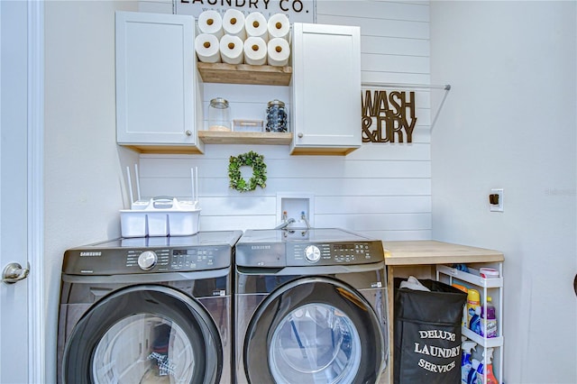 clothes washing area featuring washer and dryer, cabinets, and wooden walls