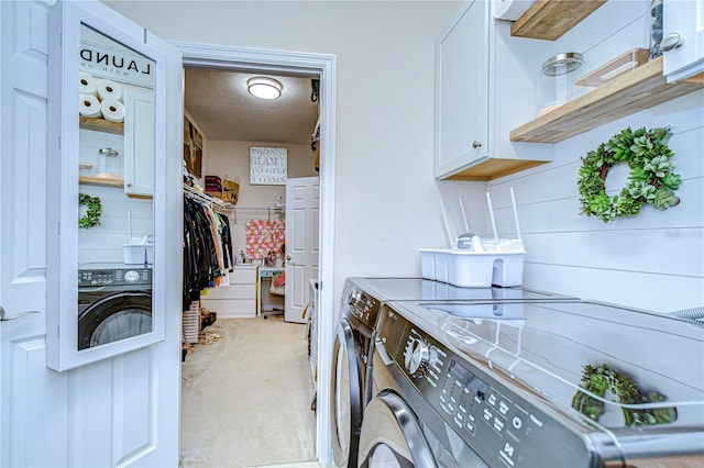 laundry room featuring washing machine and clothes dryer, cabinets, light colored carpet, and a textured ceiling