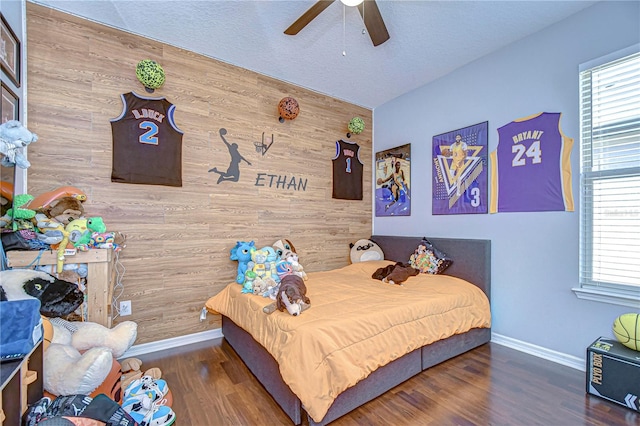 bedroom with multiple windows, wood walls, ceiling fan, and dark hardwood / wood-style floors