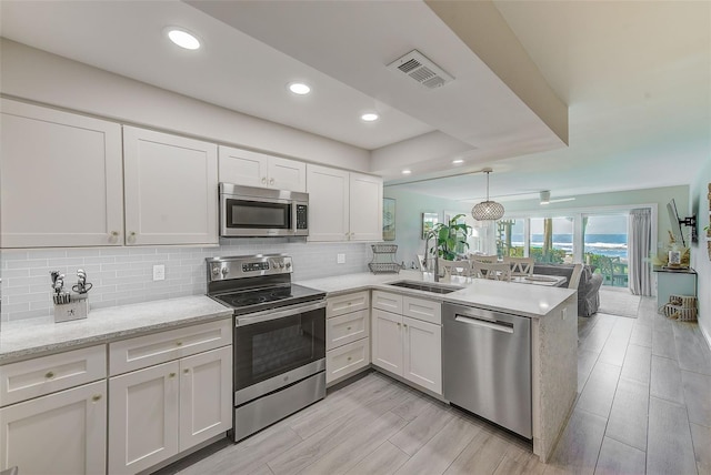 kitchen featuring decorative light fixtures, stainless steel appliances, visible vents, white cabinetry, and a peninsula