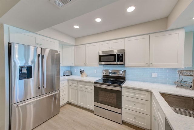 kitchen featuring light stone counters, stainless steel appliances, visible vents, backsplash, and white cabinetry