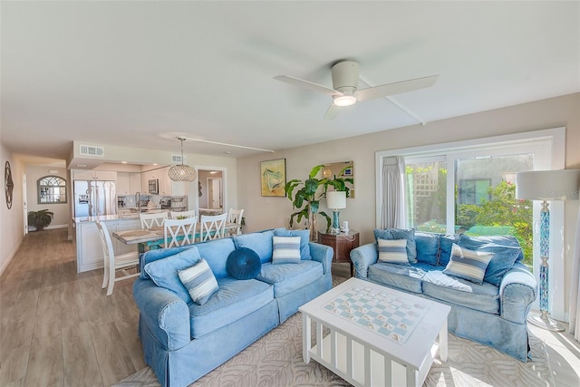 living room featuring light wood-type flooring, visible vents, and ceiling fan