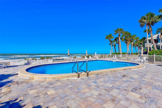 community pool featuring a patio, a water view, and fence