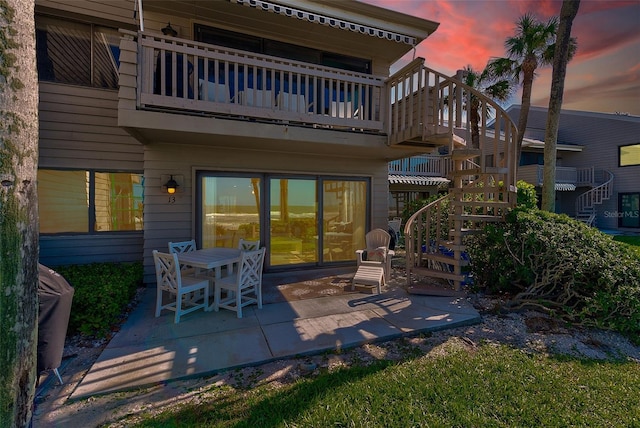 back of house at dusk with a patio, stairway, and a balcony