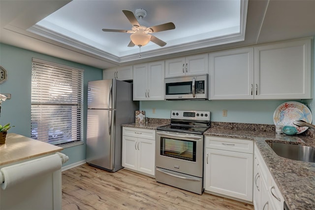 kitchen with light wood-style flooring, a sink, a tray ceiling, white cabinetry, and stainless steel appliances