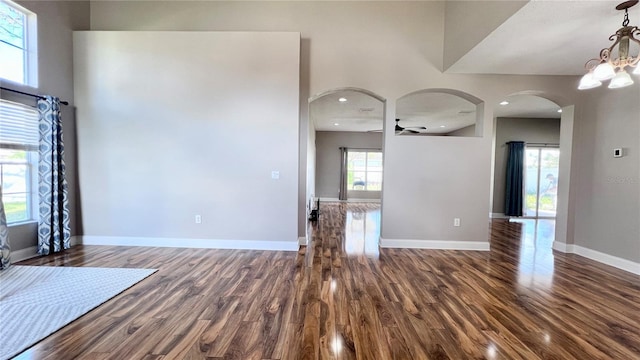 2012 Fern Ridge Ct, Holiday, FL 34691 - unfurnished living room featuring dark wood-style flooring, arched walkways, baseboards, ceiling fan, and a chandelier